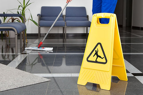 Person cleaning tiles floor with caution wet floor sign